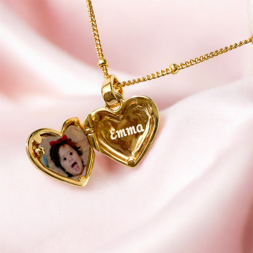 Gold heart-shaped locket with 'Emma' engraved on a pink fabric background